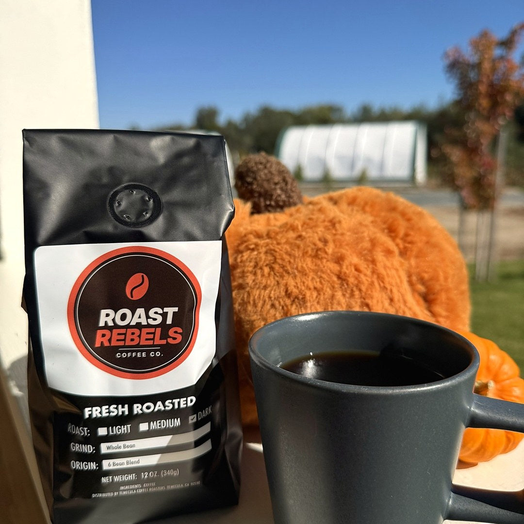Roast Rebels 6 Bean Blend bag next to a fresh cup of coffee outside on a sunny morning